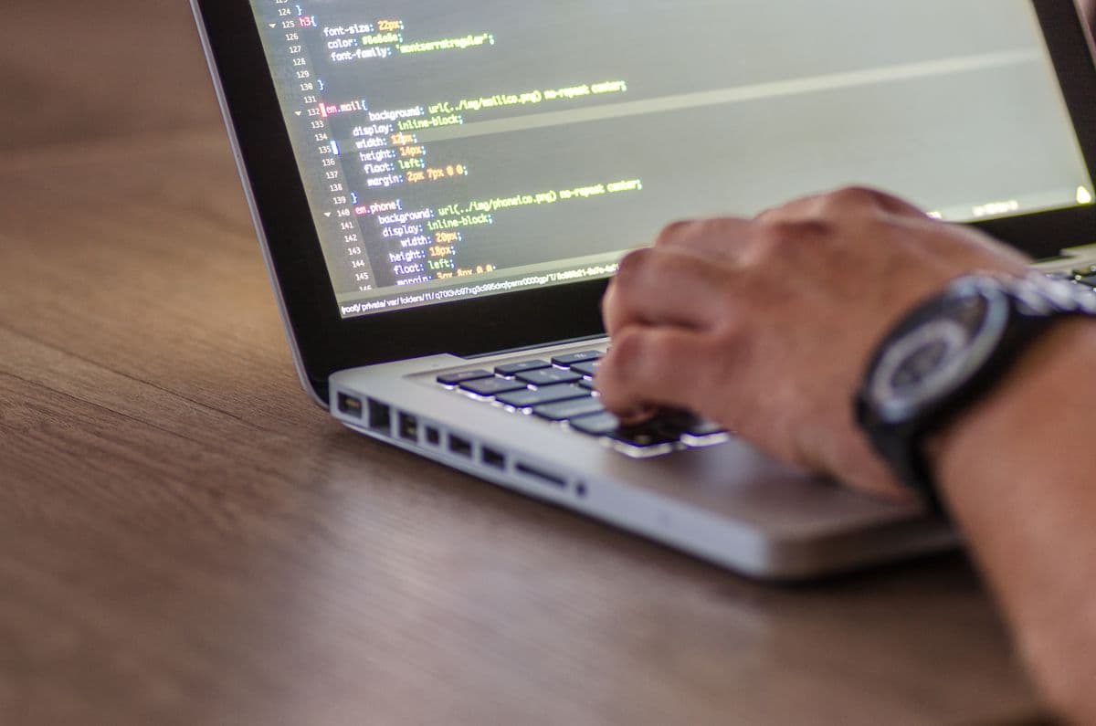 Nahaufnahme einer Hand, die auf einem Laptop mit Quellcode auf dem Bildschirm tippt